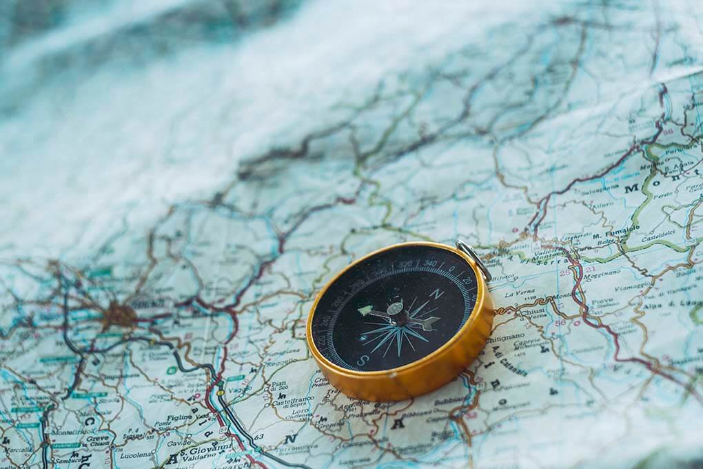 A golden compass resting on top of an open map with various geographical locations marked.